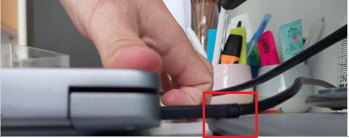 USB-C cable being compressed by raised object or monitor stand base showing obstruction causing stress on connector